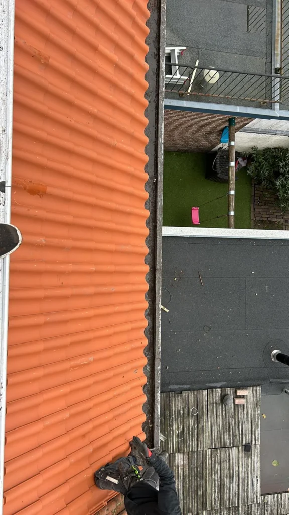Gutter between an orange tiled roof and a flat roof from above in Wolfheze